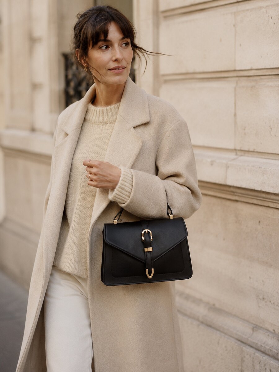 Femme en manteau crème portant un sac à main en cuir noir à fermoir doré Enna Paris, style parisien chic